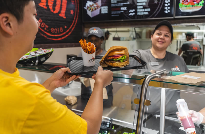 A eatery employee hands a man a meal over a counter
